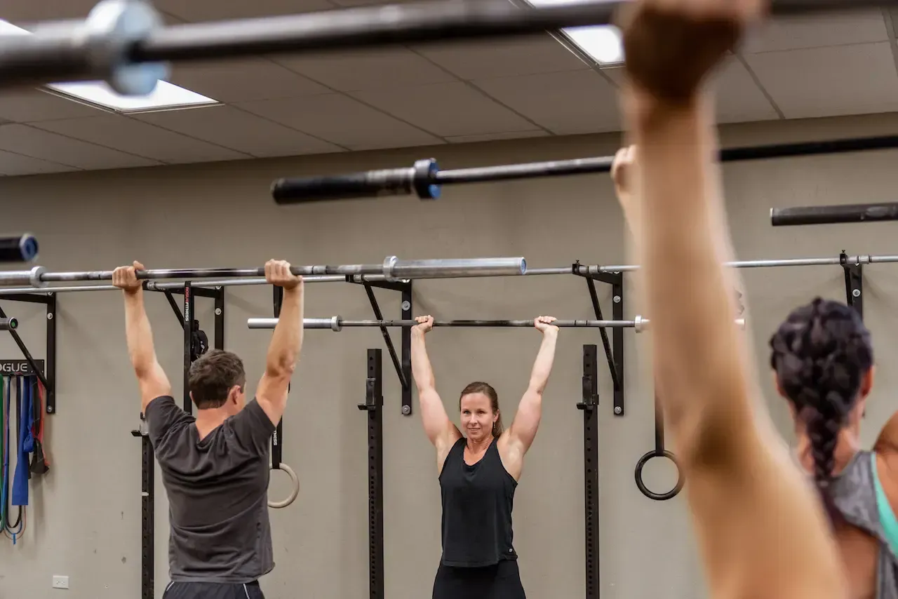 People lifting barbells overhead in a gym.