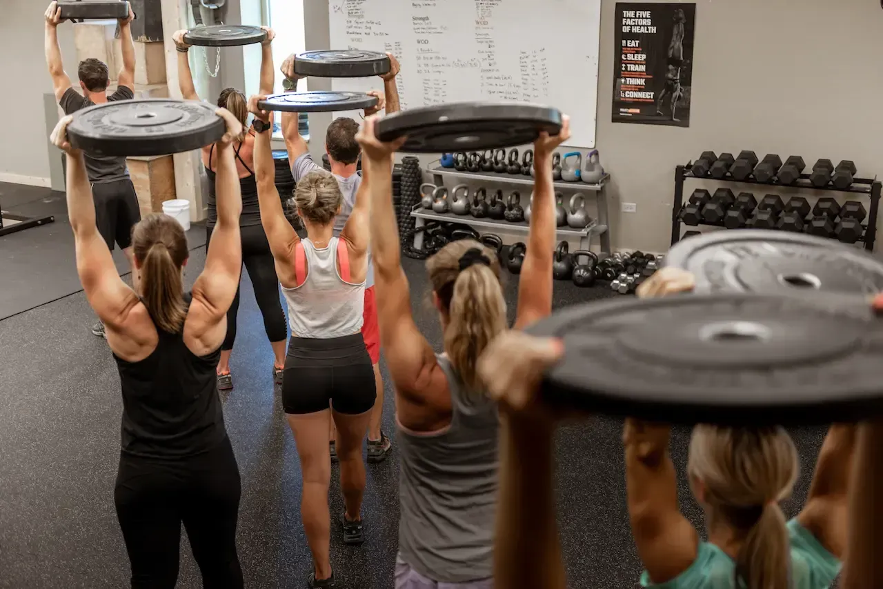 People in a gym holding weight plates above their heads.
