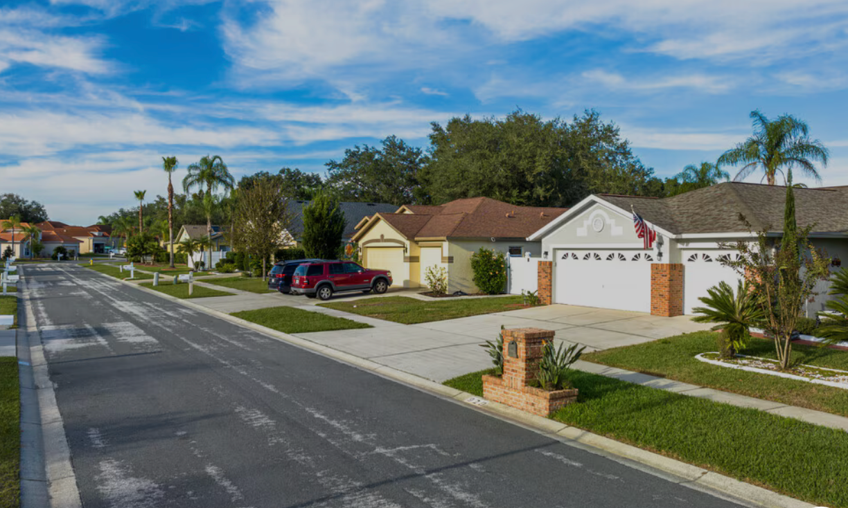 Residential street in Valrico, Florida with houses, driveways, cars, and landscaping under a blue sky.