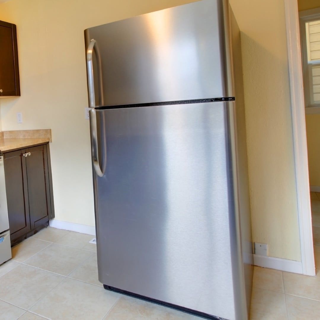 Stainless steel refrigerator in a kitchen with beige walls and tile floors.
