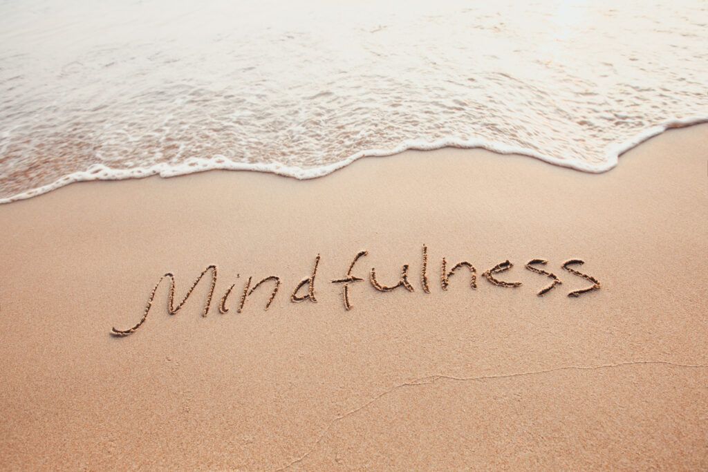 “Mindfulness” written in sand by the shoreline as waves wash in