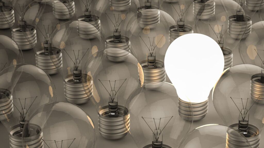 Many light bulbs, with one bright white bulb glowing among dim gray bulbs