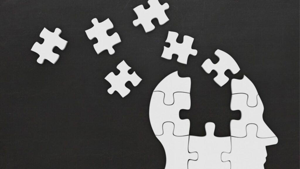 White puzzle pieces drifting toward a larger white puzzle silhouette on a dark background, symbolizing missing pieces.