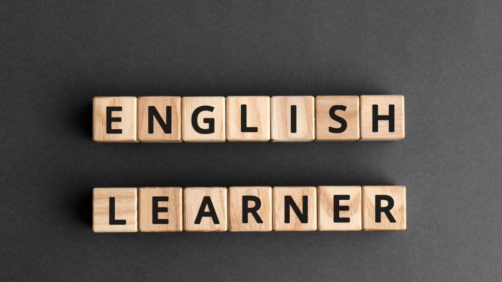 Wooden letter tiles spelling “ENGLISH LEARNER” on a dark background.