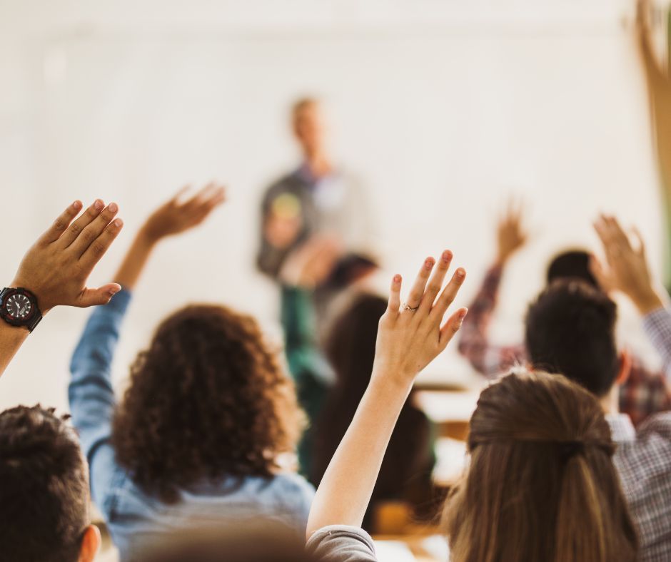 Audience raising hands in a classroom toward a blurred speaker at the front