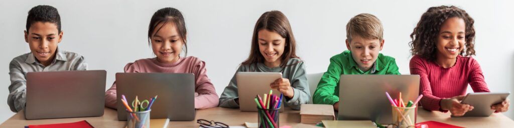 Five people using laptops at a table, smiling in a bright classroom