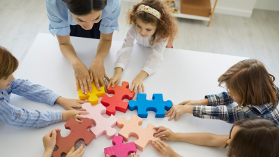 Children and an adult assembling colorful puzzle pieces together at a table