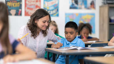 Teacher helping a student write at a classroom desk