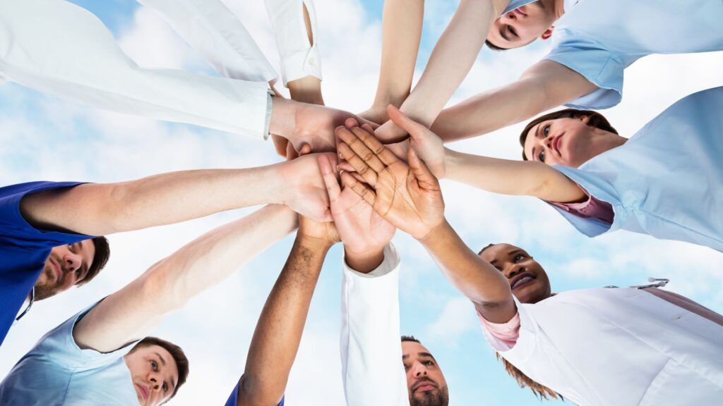 Group of people stacking hands together in a circle against a bright sky