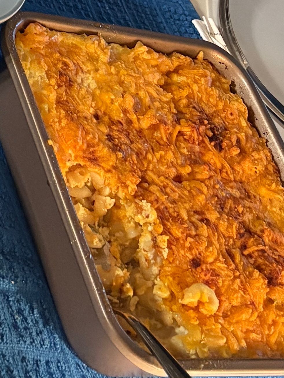 Baked casserole in a foil pan, topped with melted orange cheese on a blue cloth.