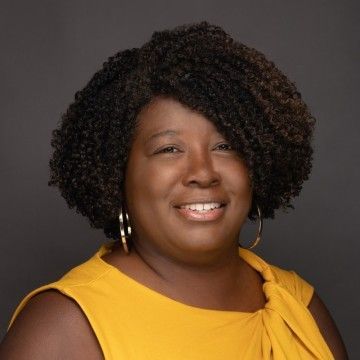 Smiling woman in a yellow top with curly hair against a dark studio background