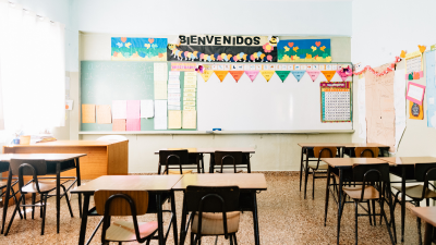 Empty classroom with desks and chairs, whiteboard, and colorful “Bienvenidos” banner above the front wall
