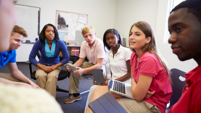 Group of students sitting in a circle, talking and working together in a classroom