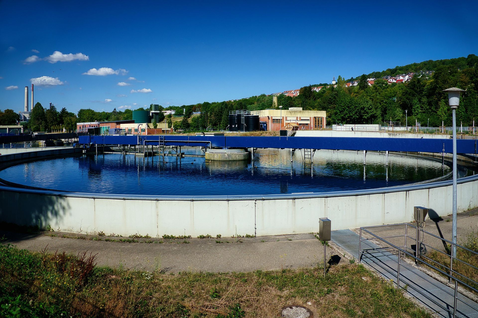Circular water tank under a blue sky, with a walkway and buildings in the background