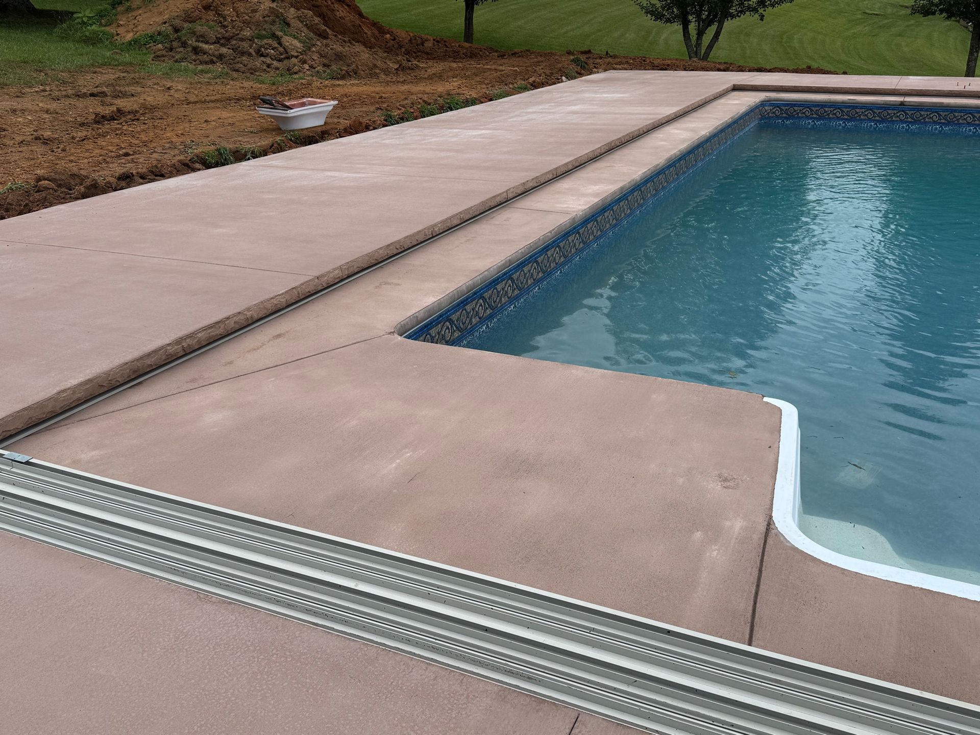 A pool deck featuring a concrete surface with installed drainage channels running along the edge of the blue water.