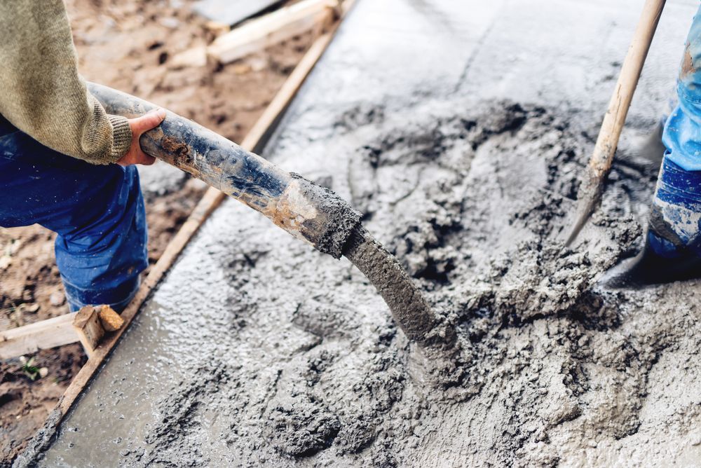 A person pours wet concrete from a hose into a wooden frame at a construction site.