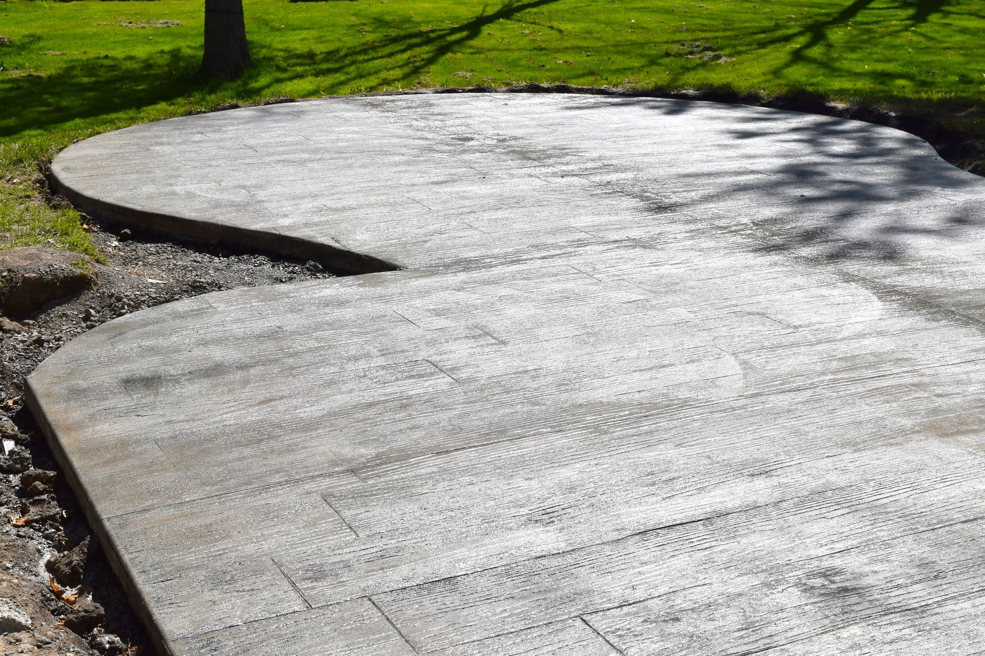 A concrete patio with a curved edge sits on the edge of a green lawn.