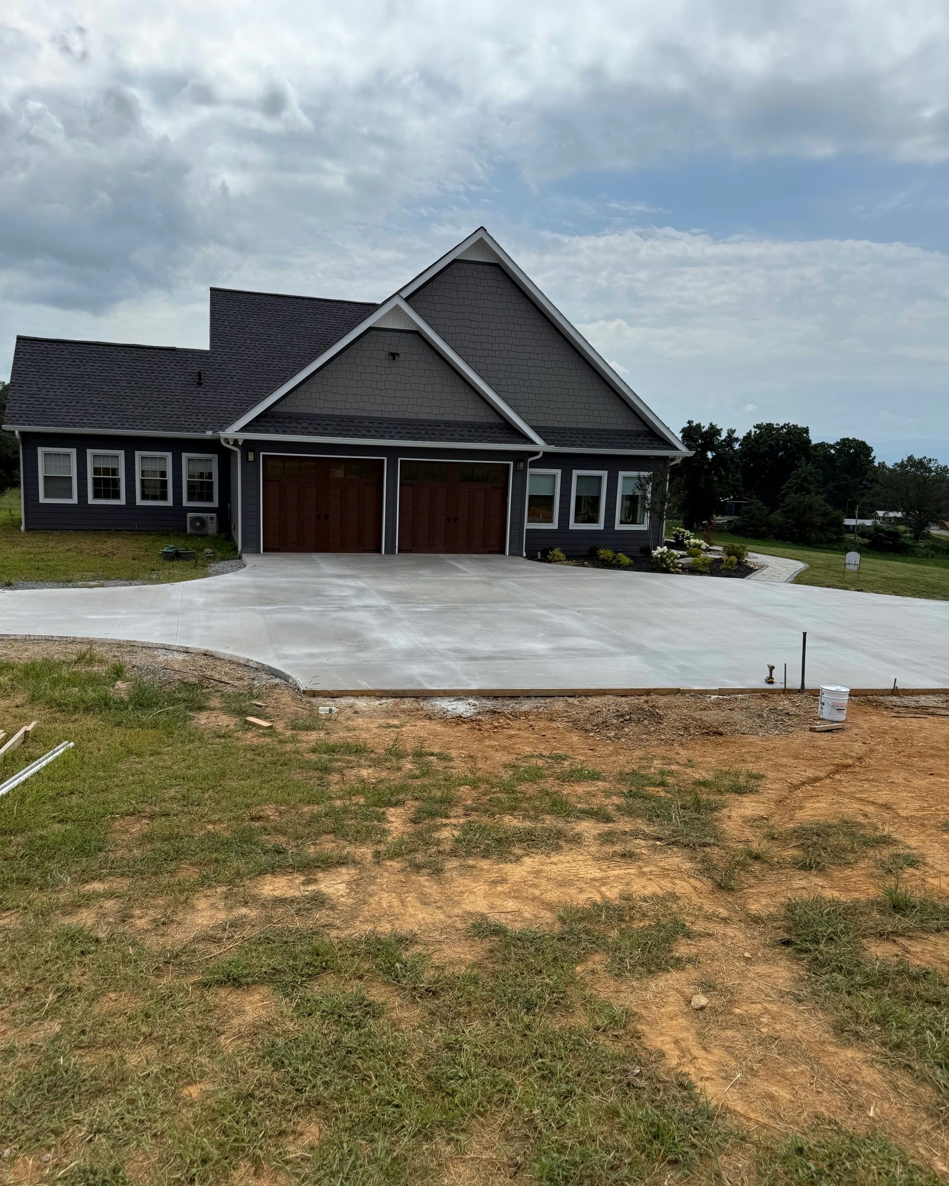 A gray house with two brown garage doors and a newly poured concrete driveway under a partly cloudy sky.