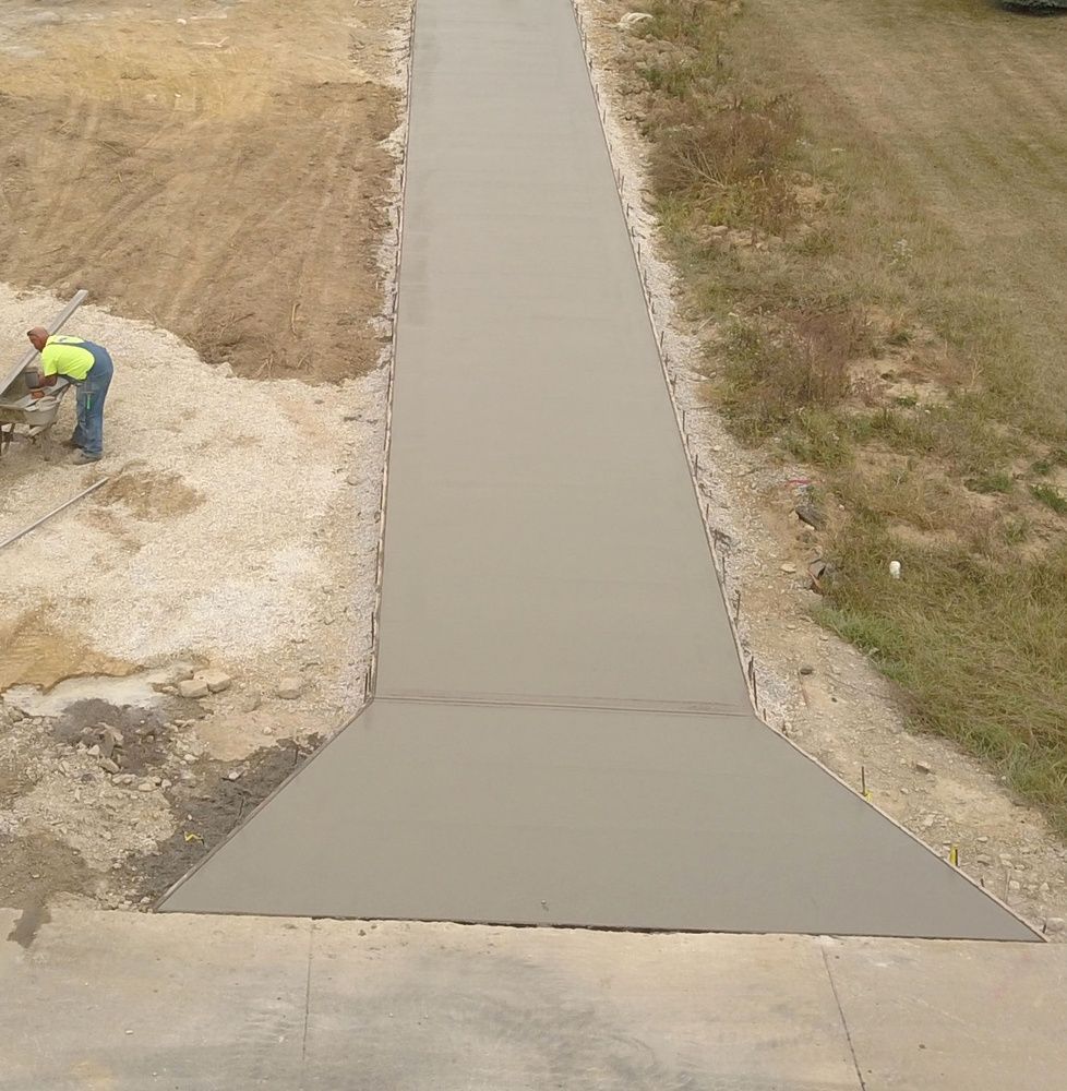 An aerial view of a construction worker smoothing freshly poured concrete for a new sidewalk extension.