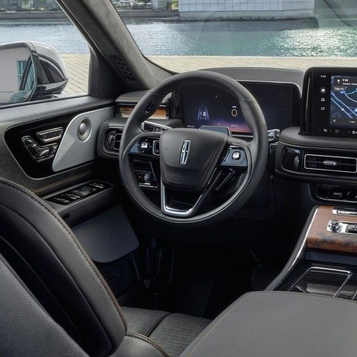 Modern car interior with black leather seats, wood trim, and a digital dashboard display