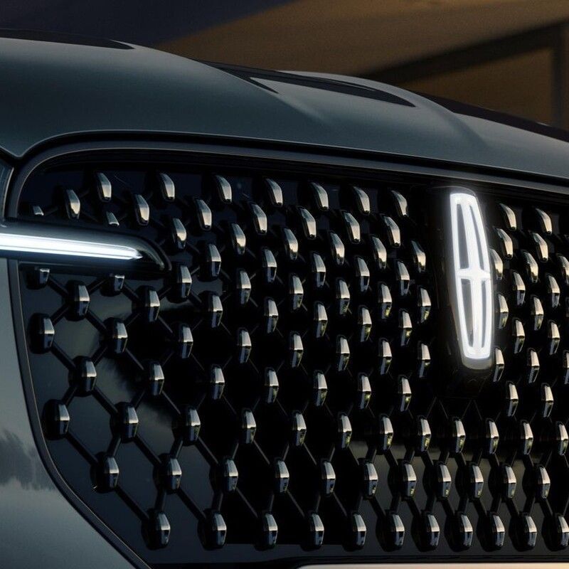 Close-up of a black luxury car front grille with illuminated LED headlights