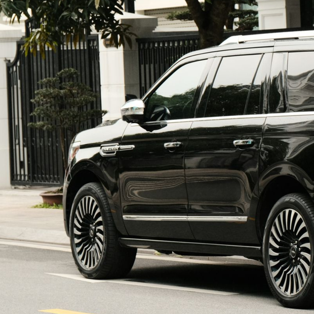 Black SUV parked on a city street beside a sidewalk and gated house