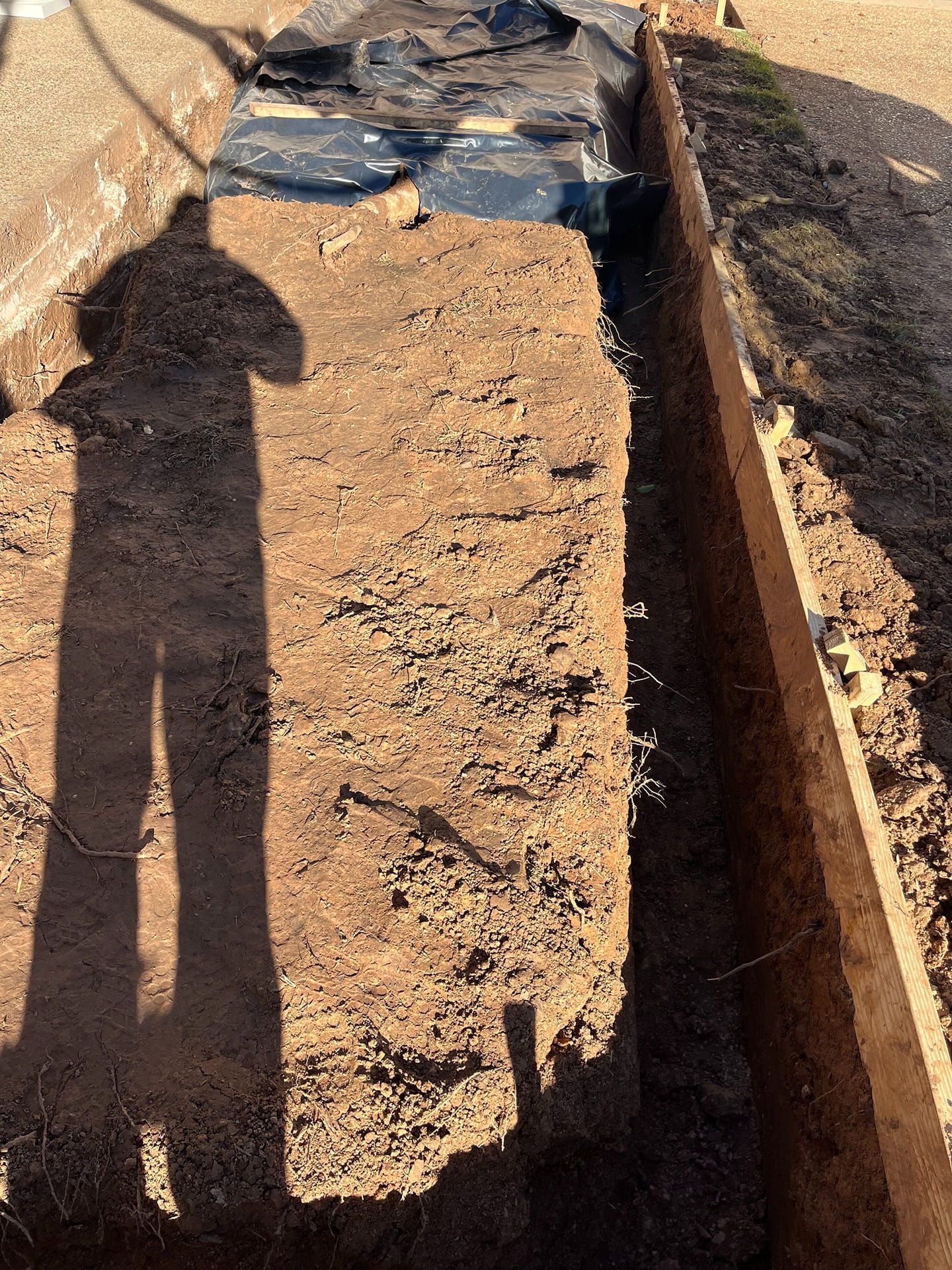 A person stands by a trench in the ground, showing a construction site with exposed soil and a covered section.