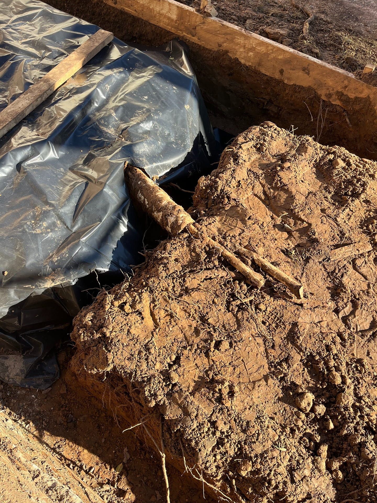 A piece of metal rebar juts out from a large mound of dirt next to a black plastic liner in a construction trench.