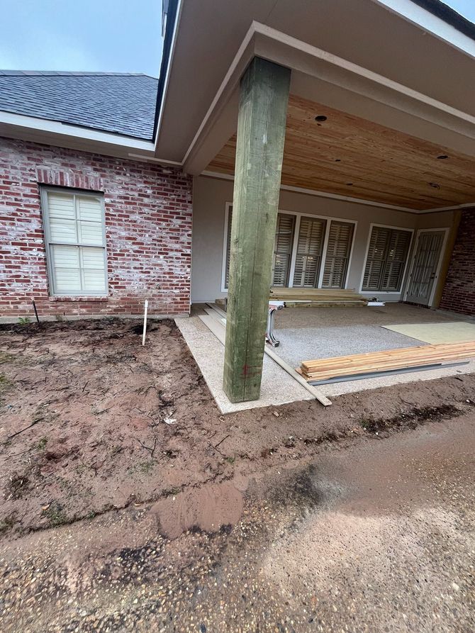 A view of a house exterior with brick walls, a wooden ceiling porch, and a large wooden support pillar under construction.