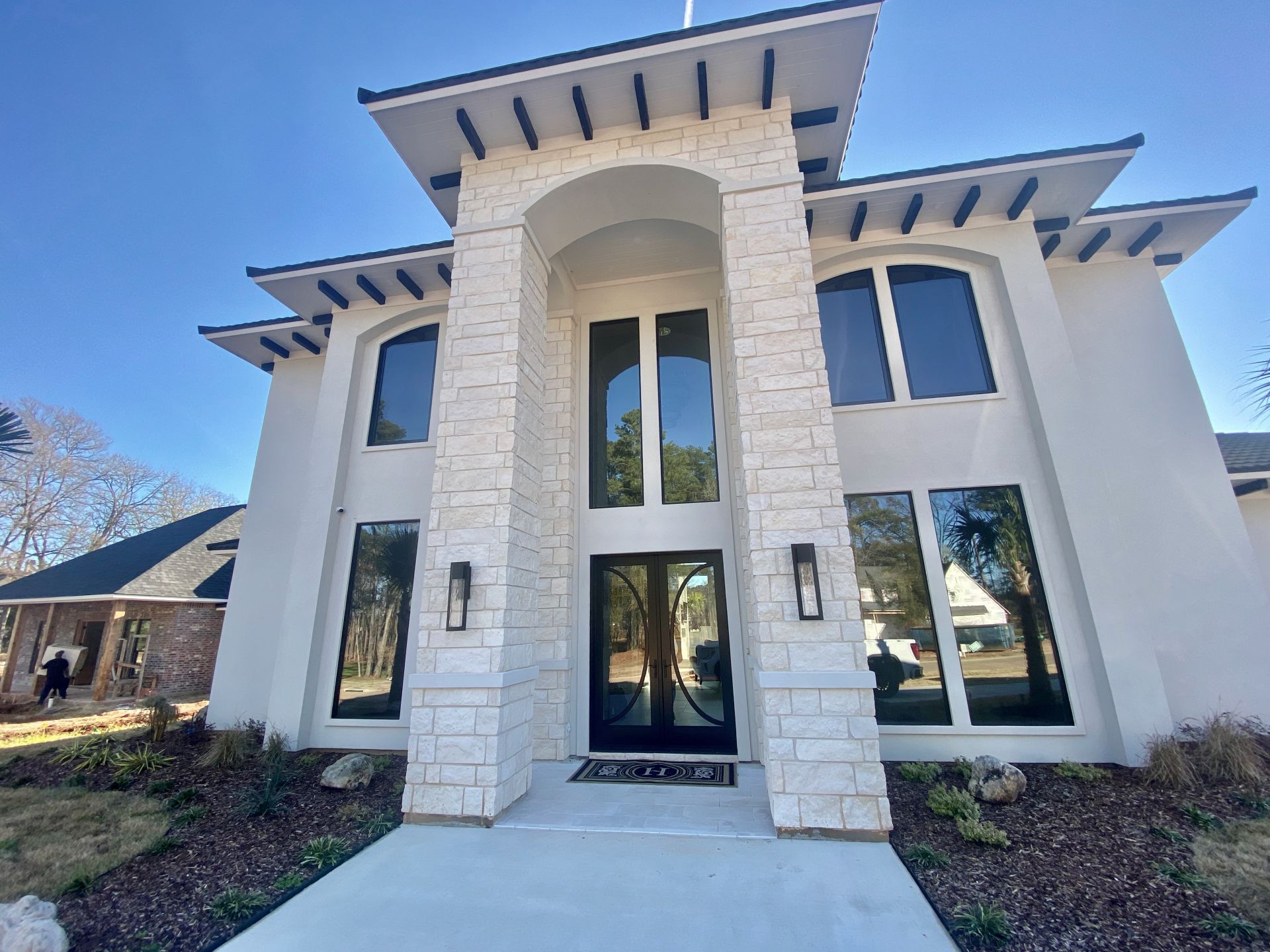 A two-story house with a white stucco facade, a stone entryway arch, a black front door, and dark-framed windows.