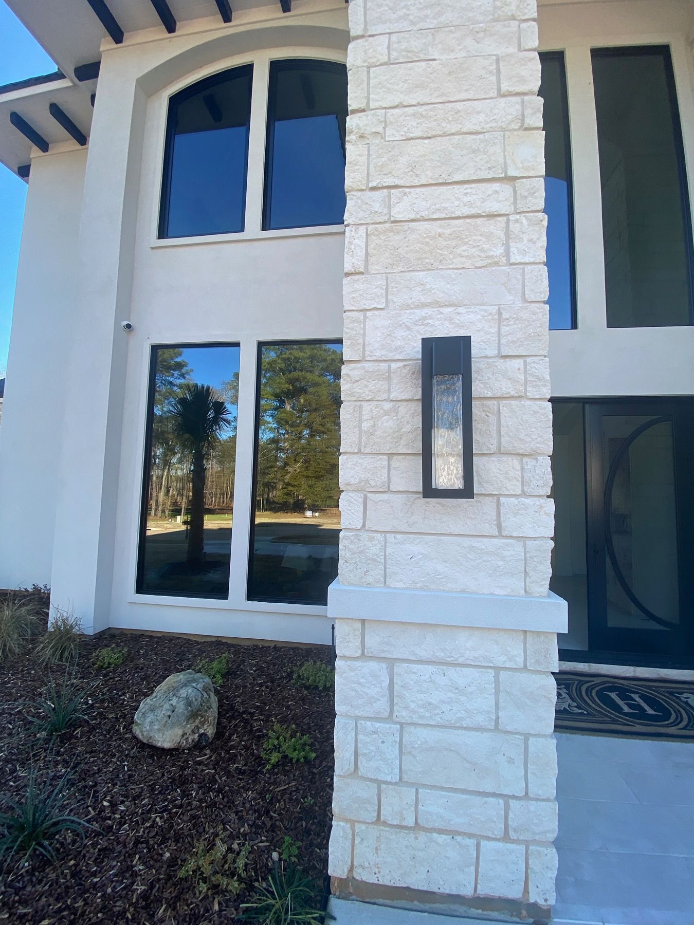 Close-up of a modern home exterior featuring cream stone masonry, tall dark-framed windows, and a black wall sconce.