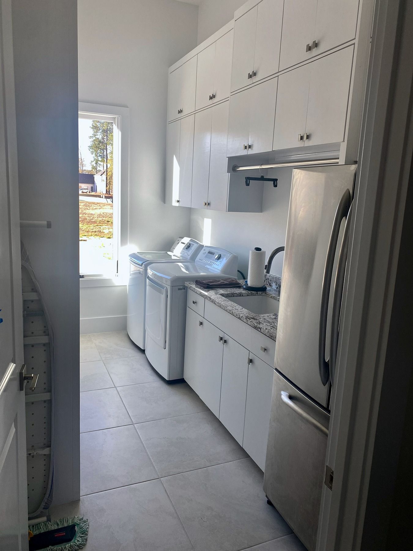 White laundry room with a washer and dryer, speckled countertop, sink, stainless steel refrigerator, and wall cabinets.