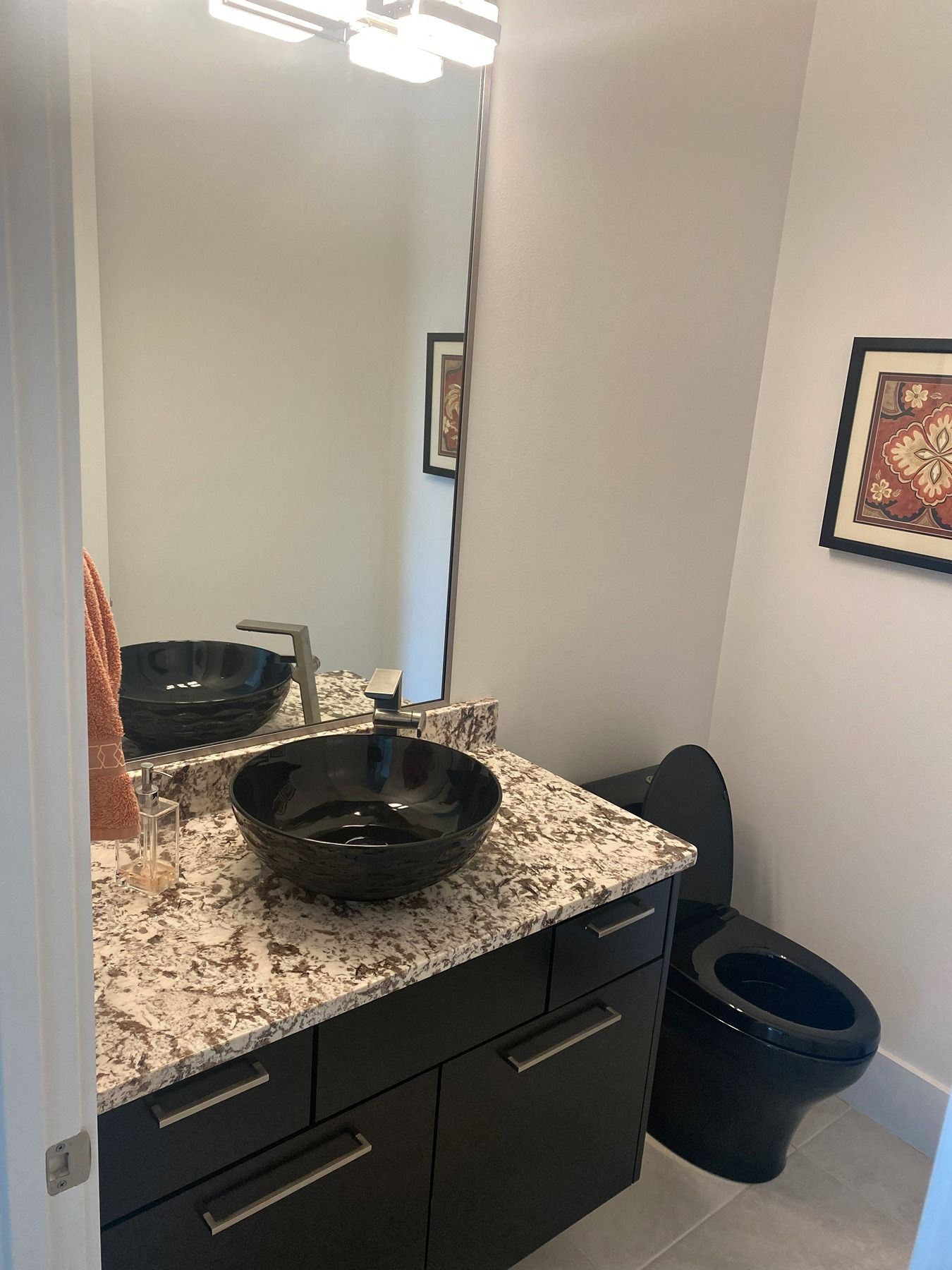 Modern half bathroom with a black vessel sink, granite countertop, black vanity, and black toilet.