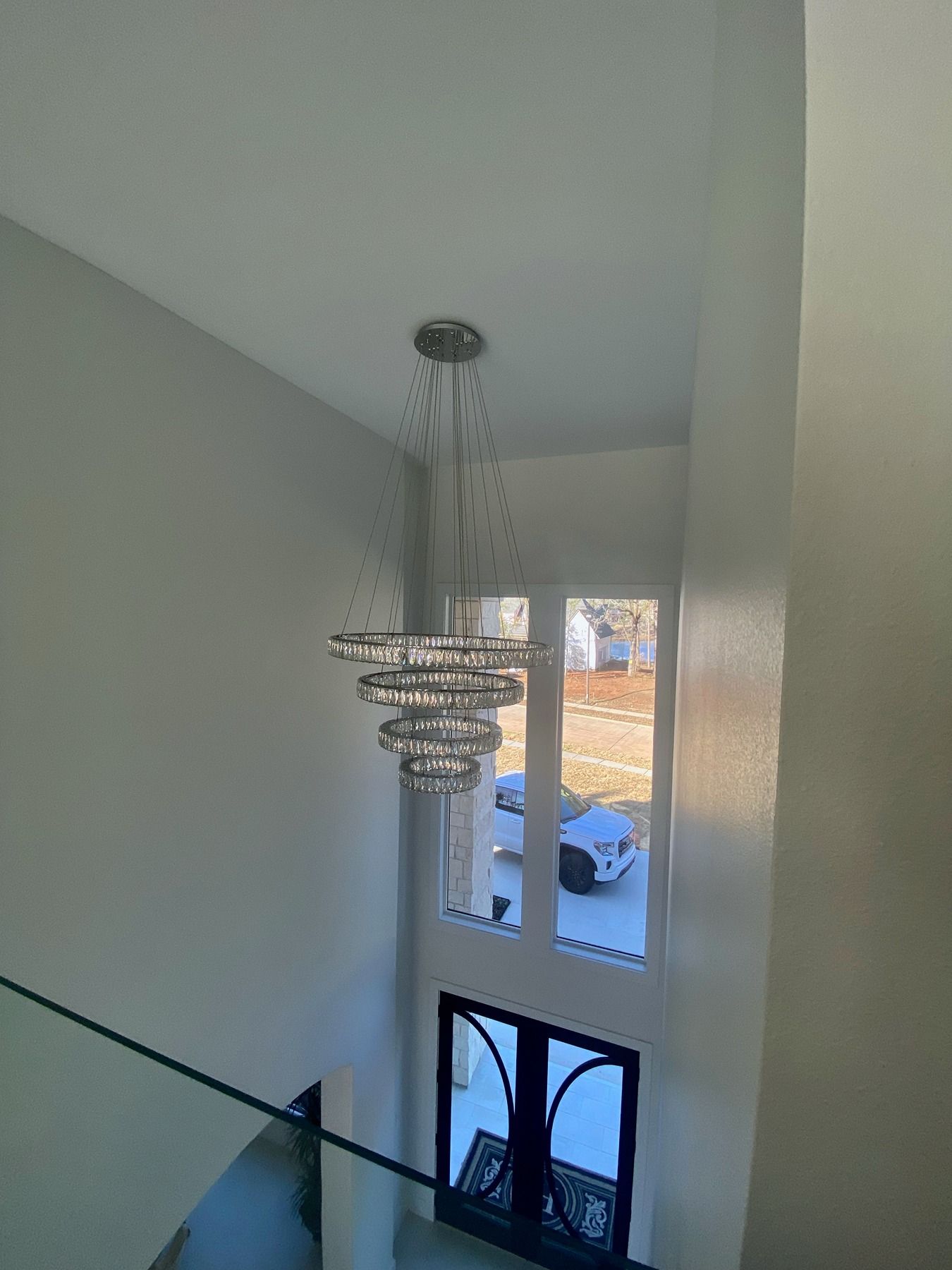A multi-tiered crystal chandelier hangs in an entryway viewed from a staircase overlooking the front door.