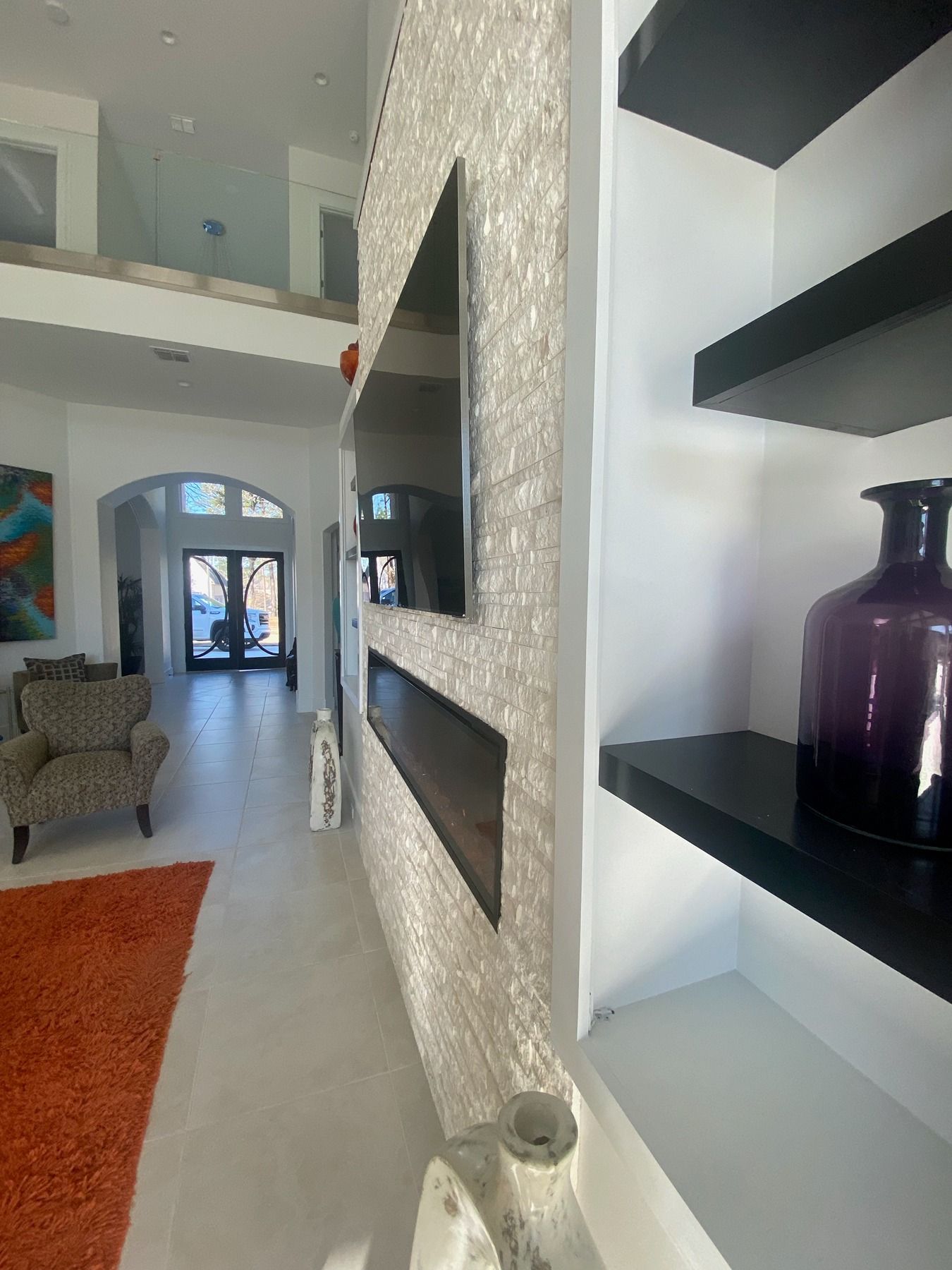A wall with a white textured finish, mounted TV, and fireplace, with black shelves holding a purple vase to the right.