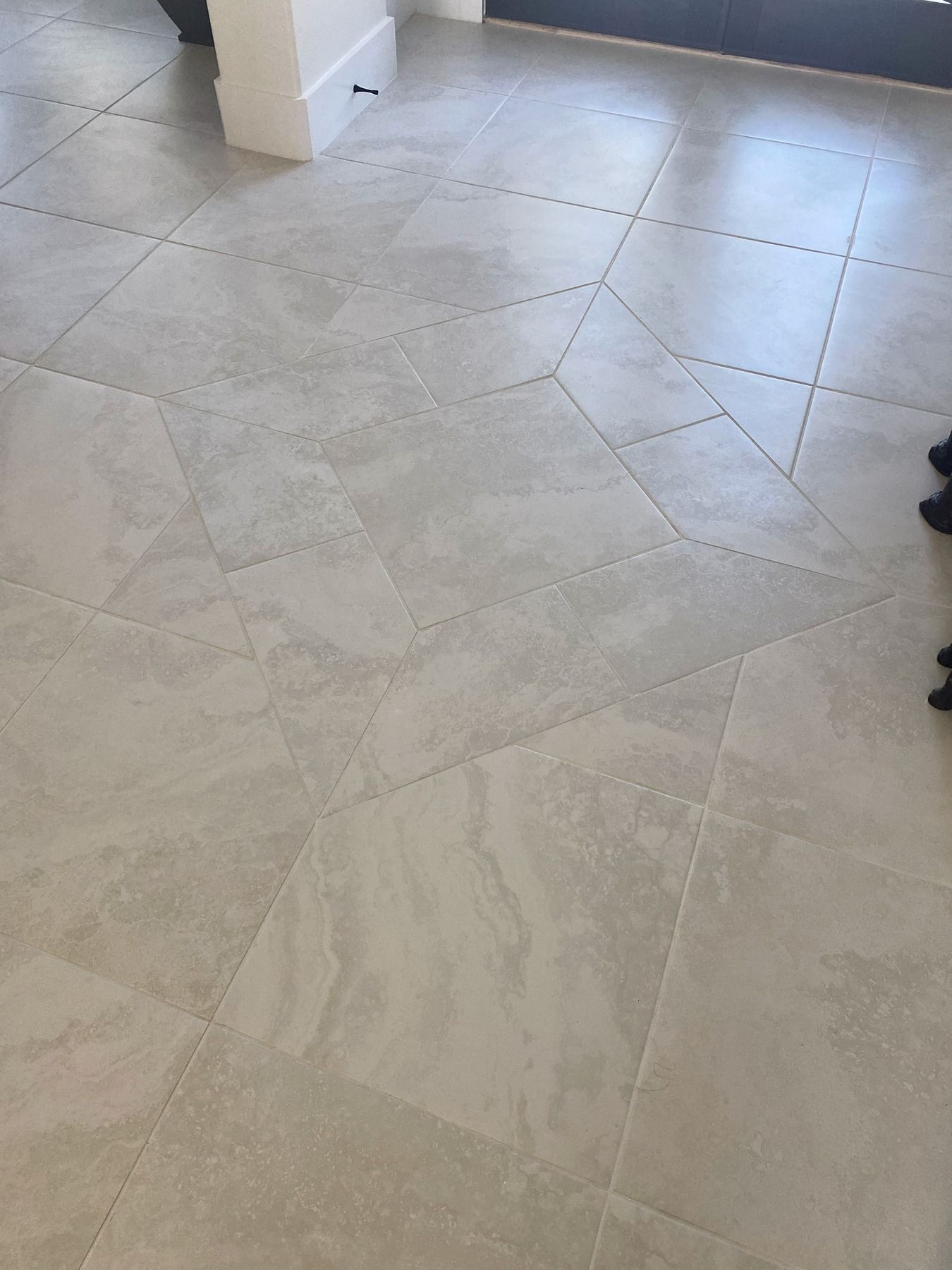 A close-up of a light beige stone-look tile floor with a geometric pattern created by tiles of varying sizes.