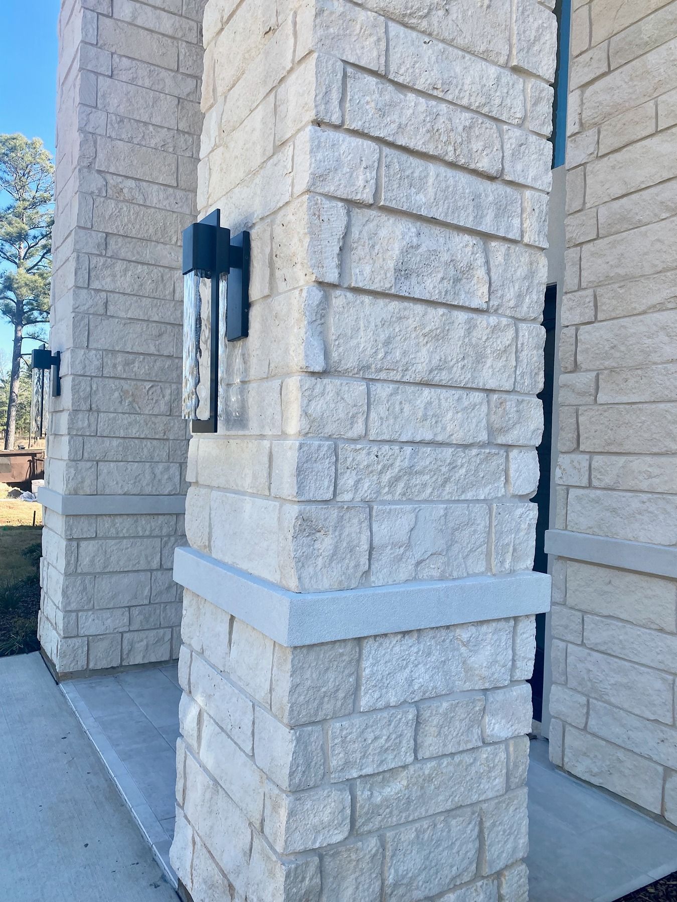 Light-colored stone columns with integrated black wall-mounted lights framing a building entryway.