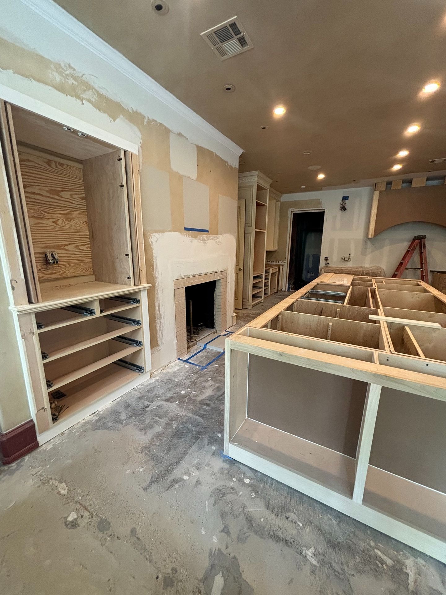 An unfinished kitchen renovation featuring raw wood cabinetry, a fireplace, a large island, and exposed drywall.