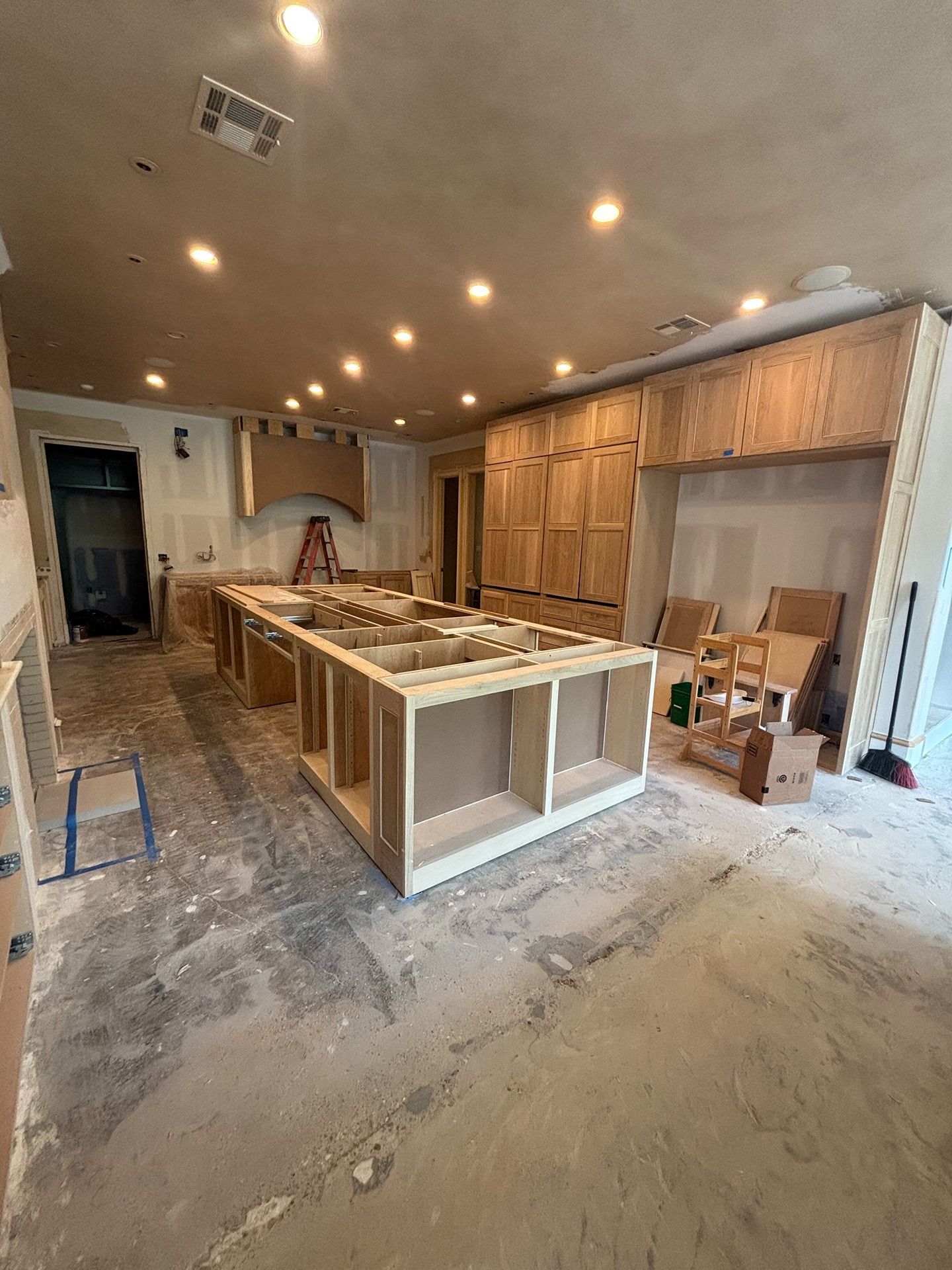 Kitchen under construction with an unfinished wooden island and cabinets, exposed drywall, and recessed lighting.