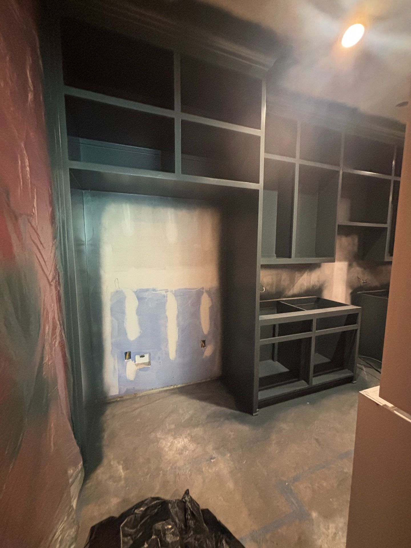Newly installed dark gray kitchen cabinetry in an unfinished room with drywall and a concrete floor.
