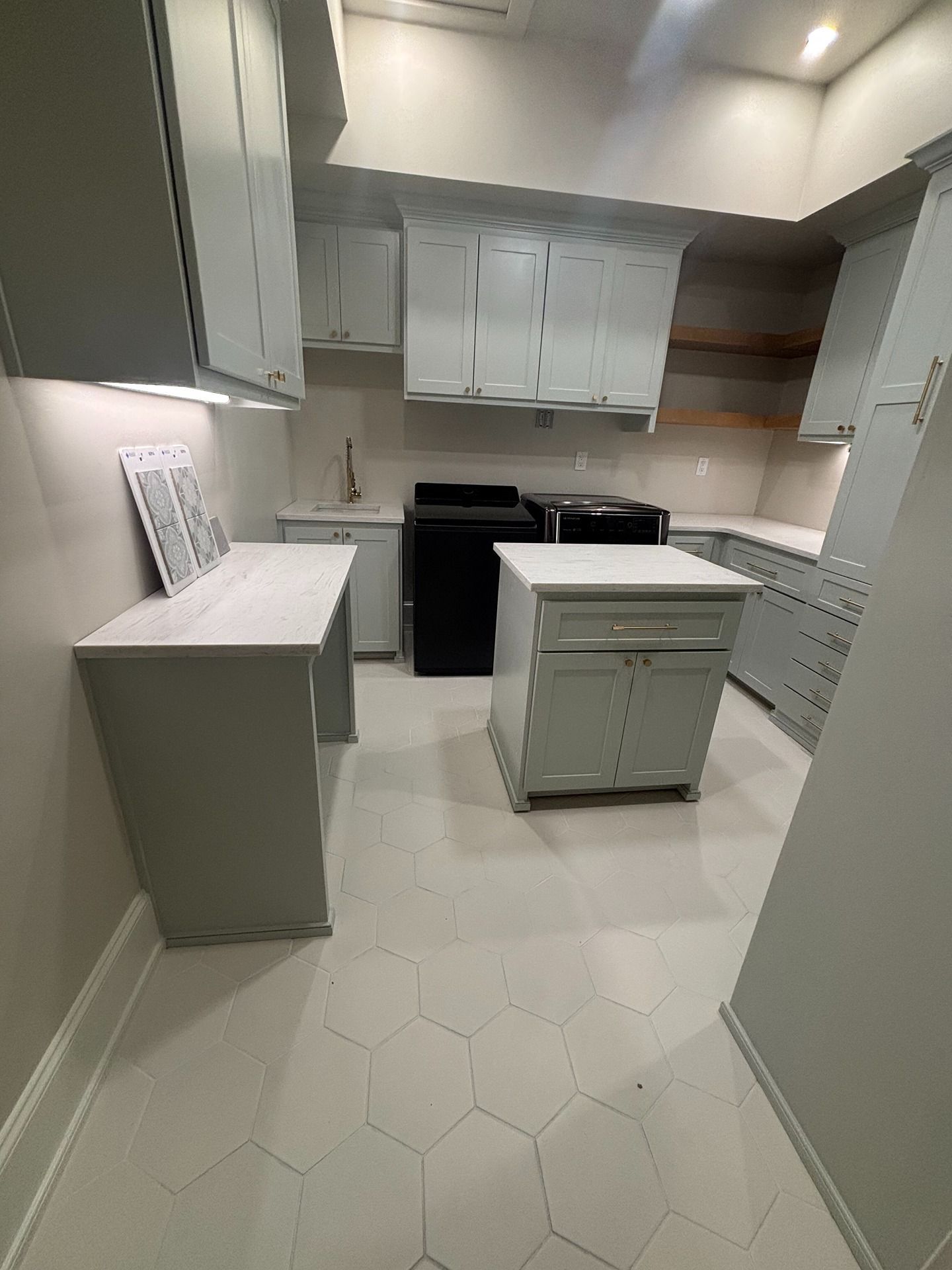 A modern kitchen featuring light gray cabinets, white countertops, black appliances, and white hexagonal floor tiles.