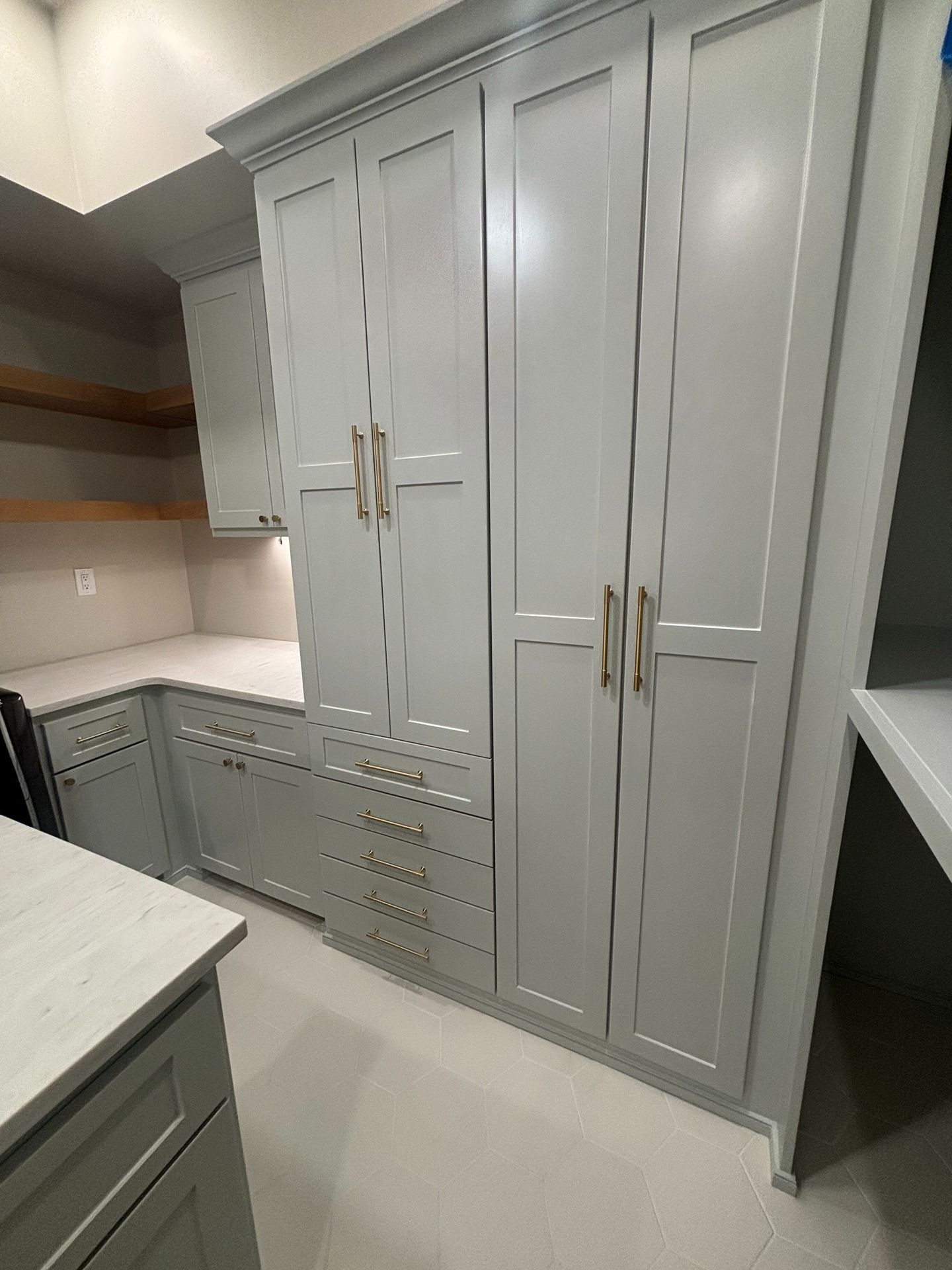 Tall, light gray kitchen cabinets featuring shaker-style doors, brass hardware, and a base cabinet with lower drawers.