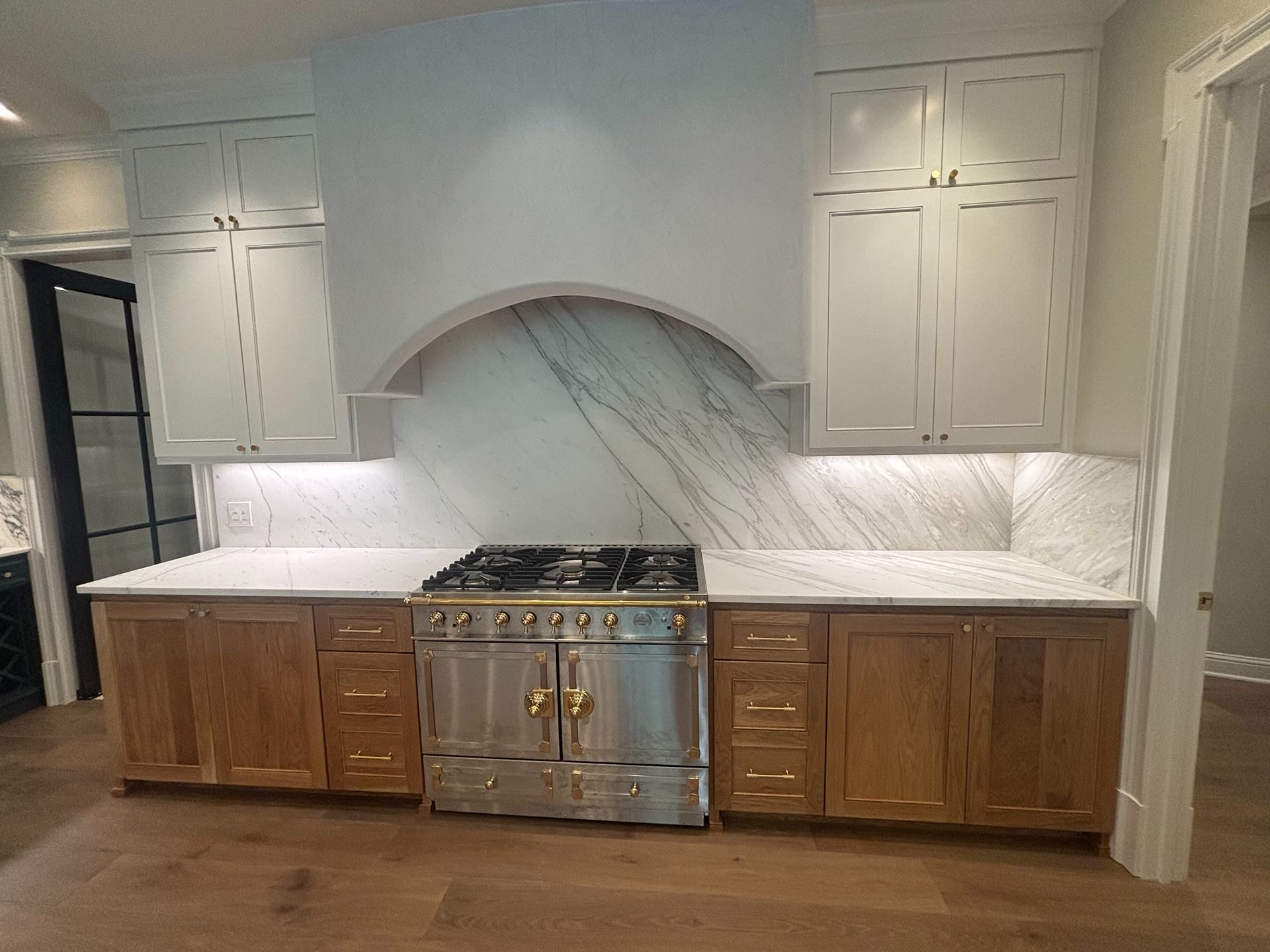 A kitchen with white upper cabinets, light wood lower cabinets, a stainless steel gas range, and a marble backsplash.