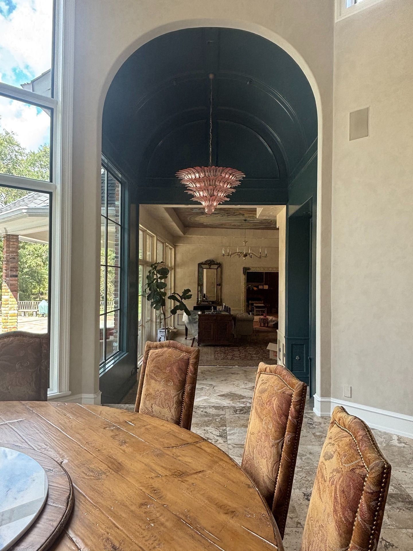 A dining room leads into a hallway with a dark arched ceiling, a tiered chandelier, and a view into a living area.
