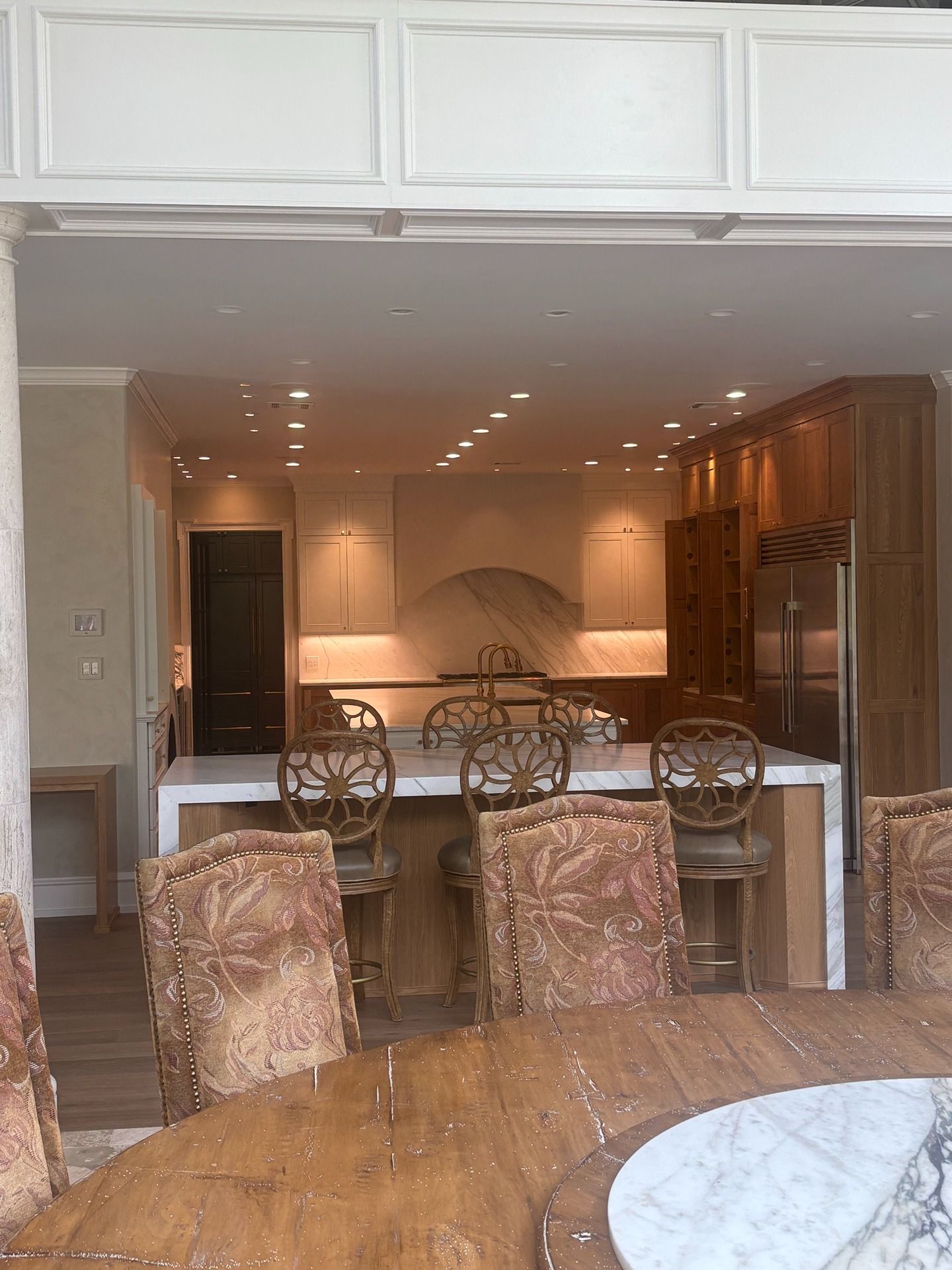 A dining area in the foreground leads into a kitchen with wood cabinetry, a white island, and decorative chairs.