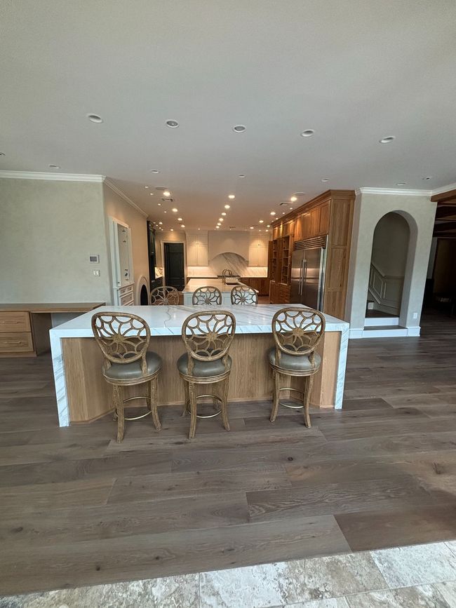 A modern kitchen island with three ornate metal bar stools, wood cabinetry, and white countertops in an open floor plan.