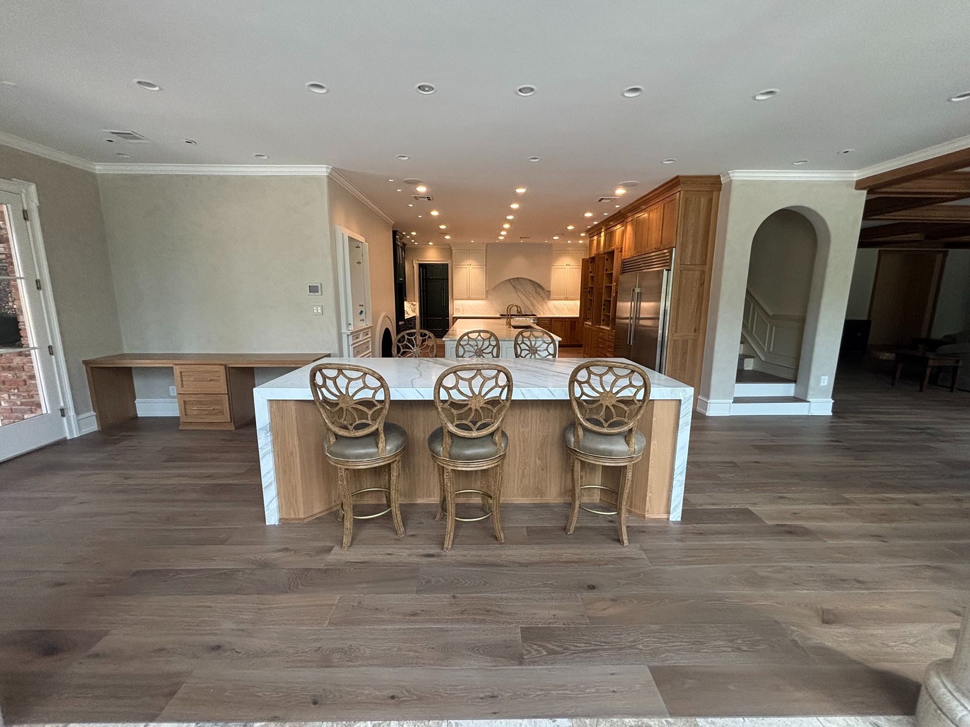 A modern kitchen with a white-topped island, three ornate stools, and light wood cabinetry on a hardwood floor.