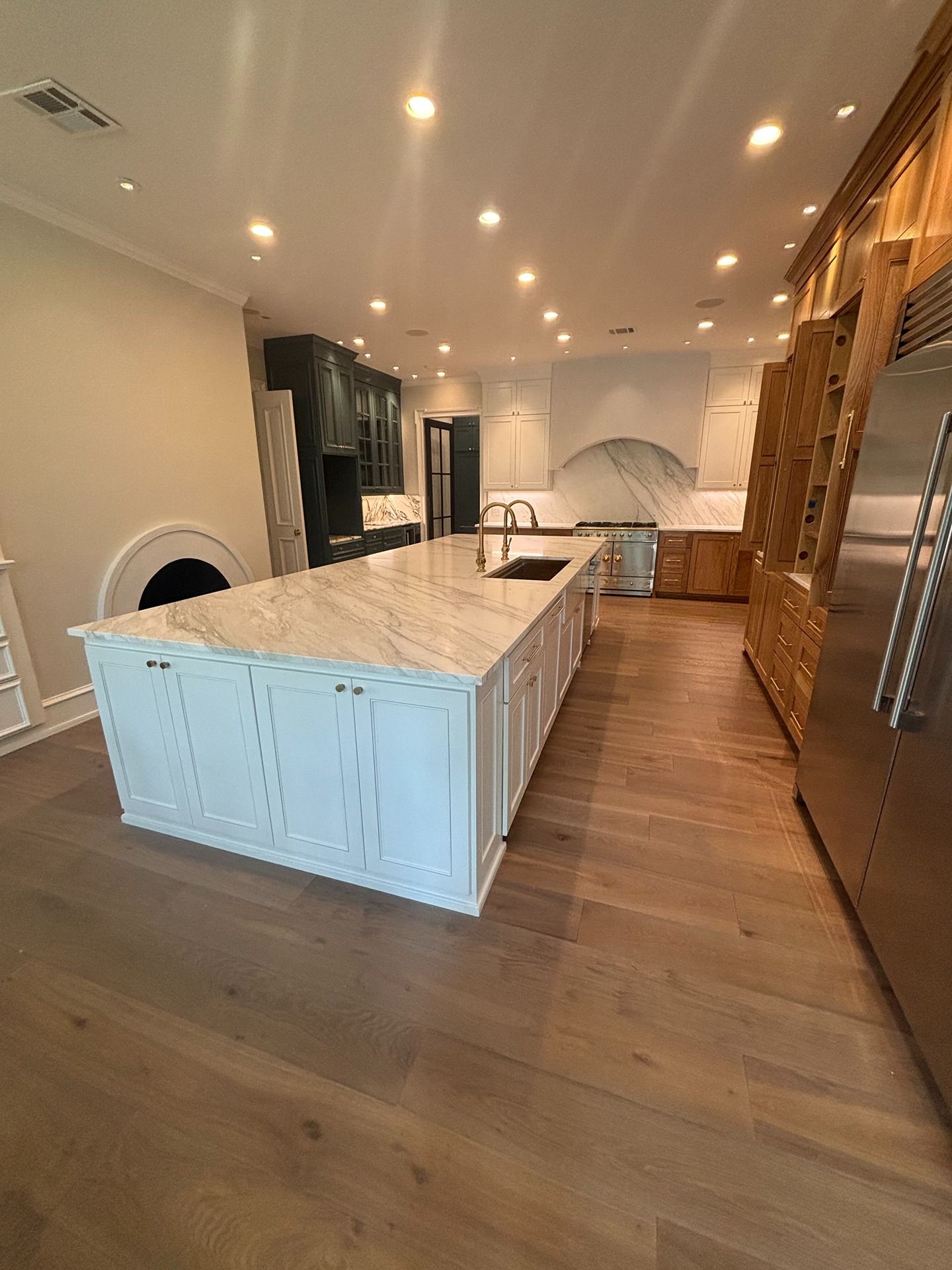 A bright, spacious kitchen featuring a large white marble island, light wood floors, dark cabinetry, and recessed lighting.