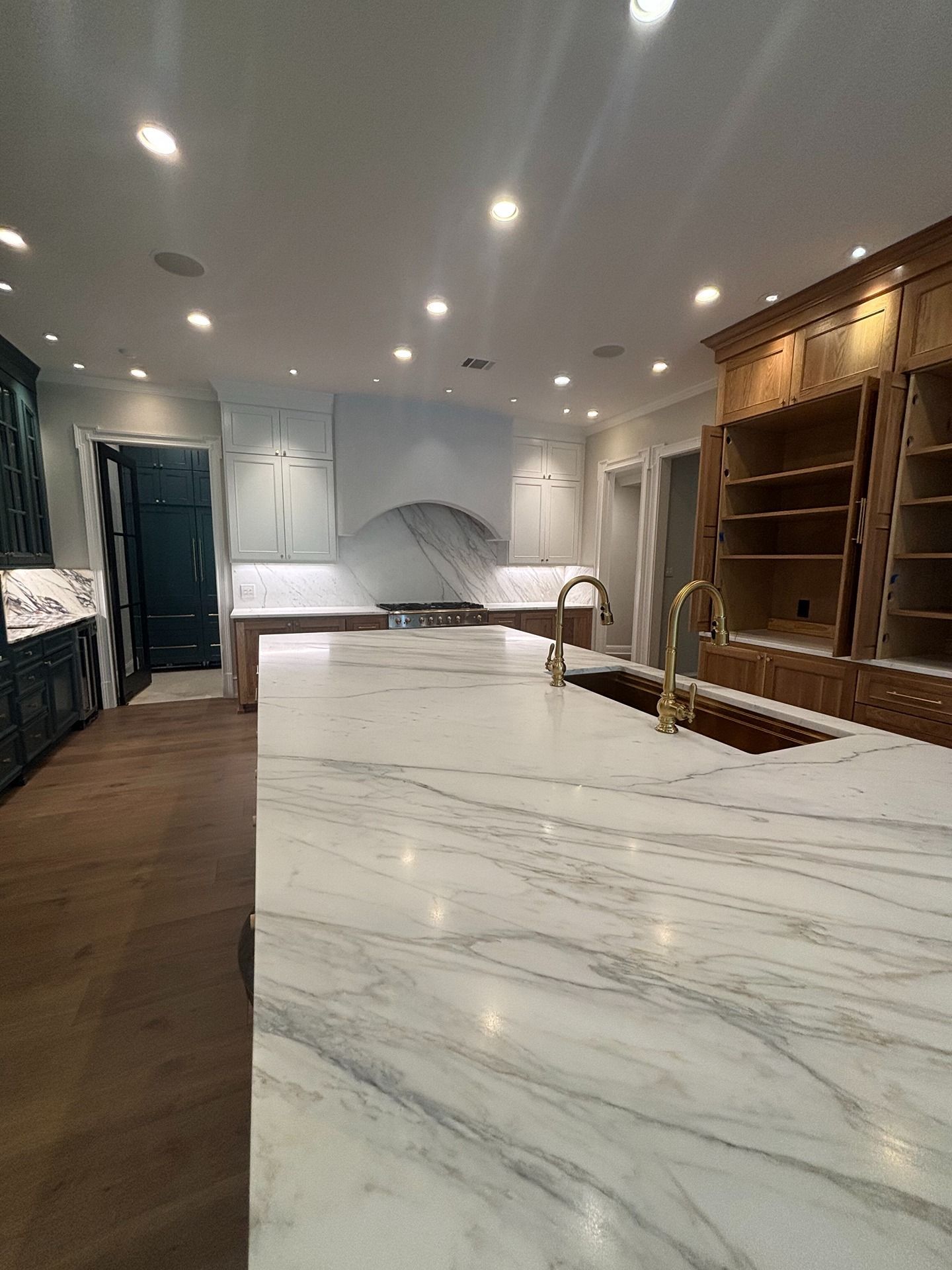 A modern kitchen featuring a large white marble-topped island, wooden cabinetry, and blue accents under recessed lighting.