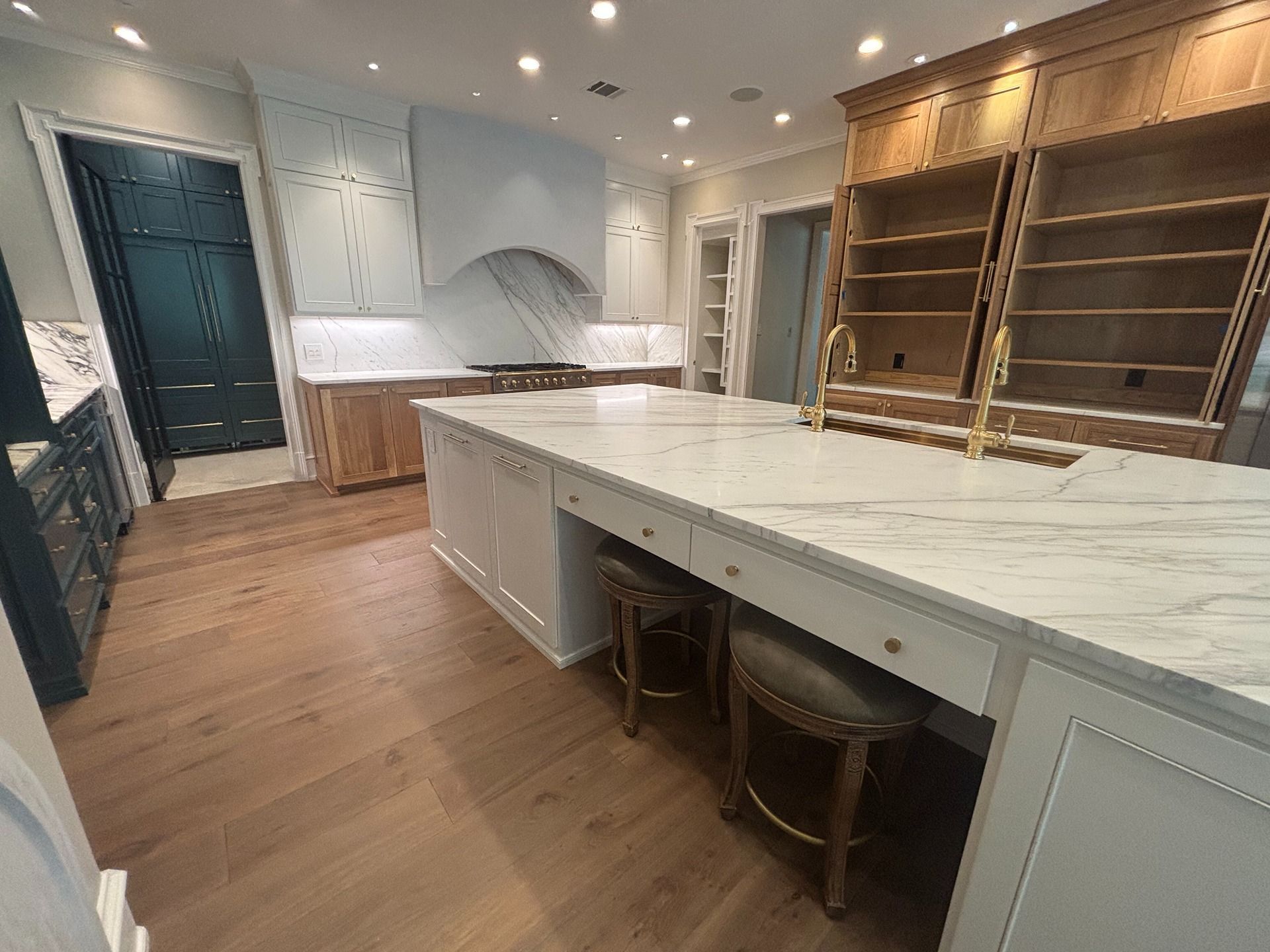 A bright, modern kitchen featuring a large white marble island, light wood cabinetry, and a dark blue paneled doorway.